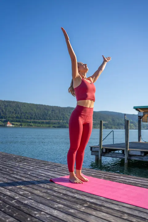 Frau macht Yoga in der Sonne am Steg vom Woerthersee